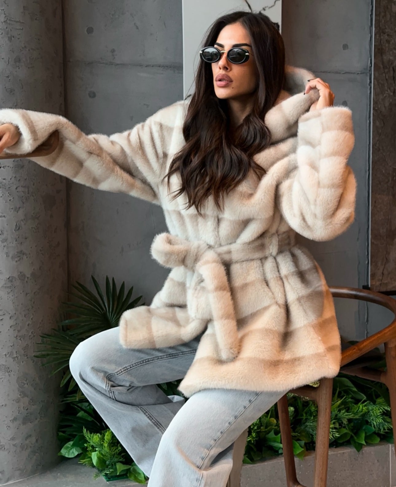 Pelliccia GEMMA Realizzato in pelliccia di visone ecologico di alta qualità, presenta una texture morbida e avvolgente con lavorazione a fasce orizzontali. Il design è arricchito da cappuccio e cintura in coordinato