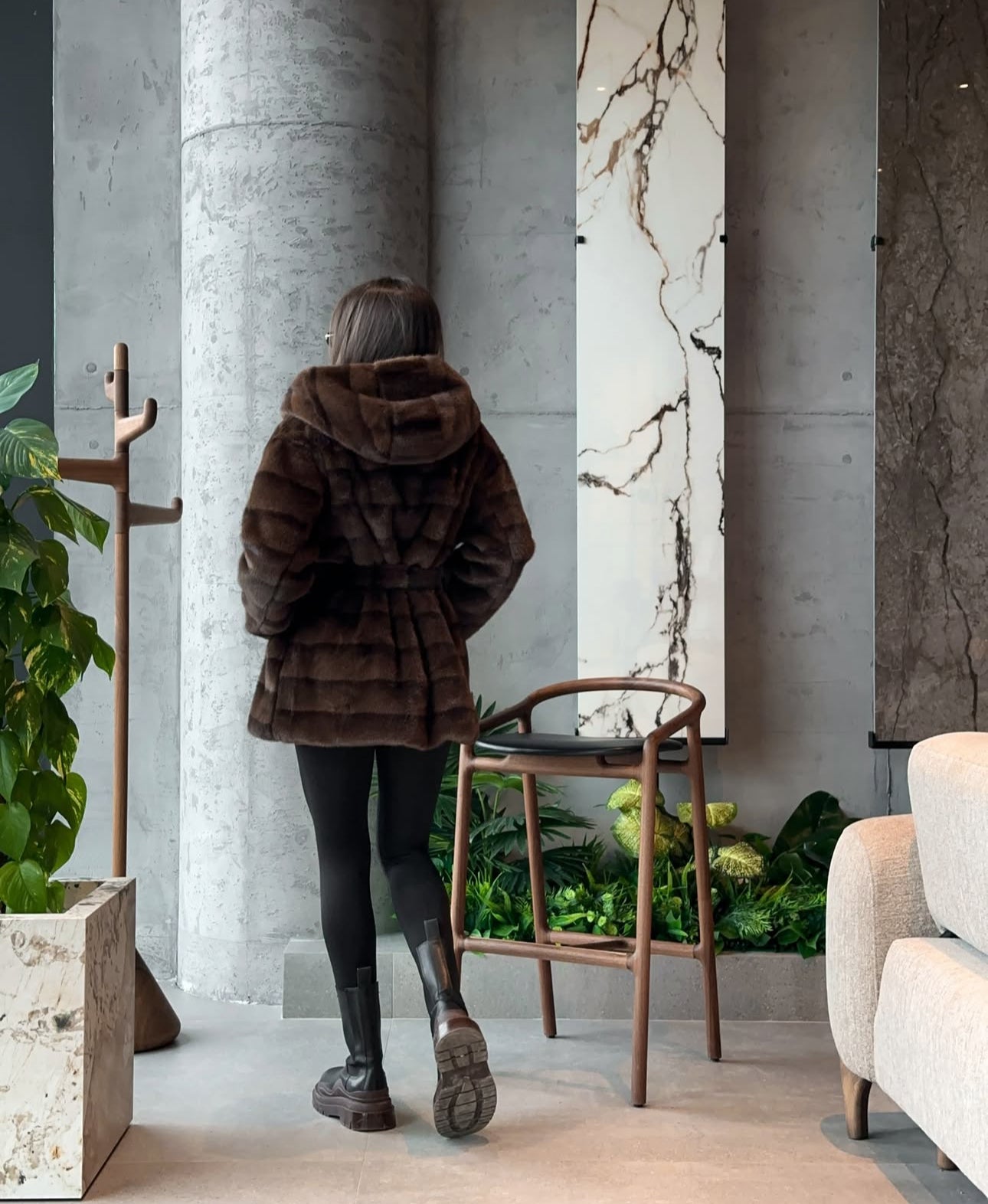 Pelliccia GEMMA Realizzato in pelliccia di visone ecologico di alta qualità, presenta una texture morbida e avvolgente con lavorazione a fasce orizzontali. Il design è arricchito da cappuccio e cintura in coordinato