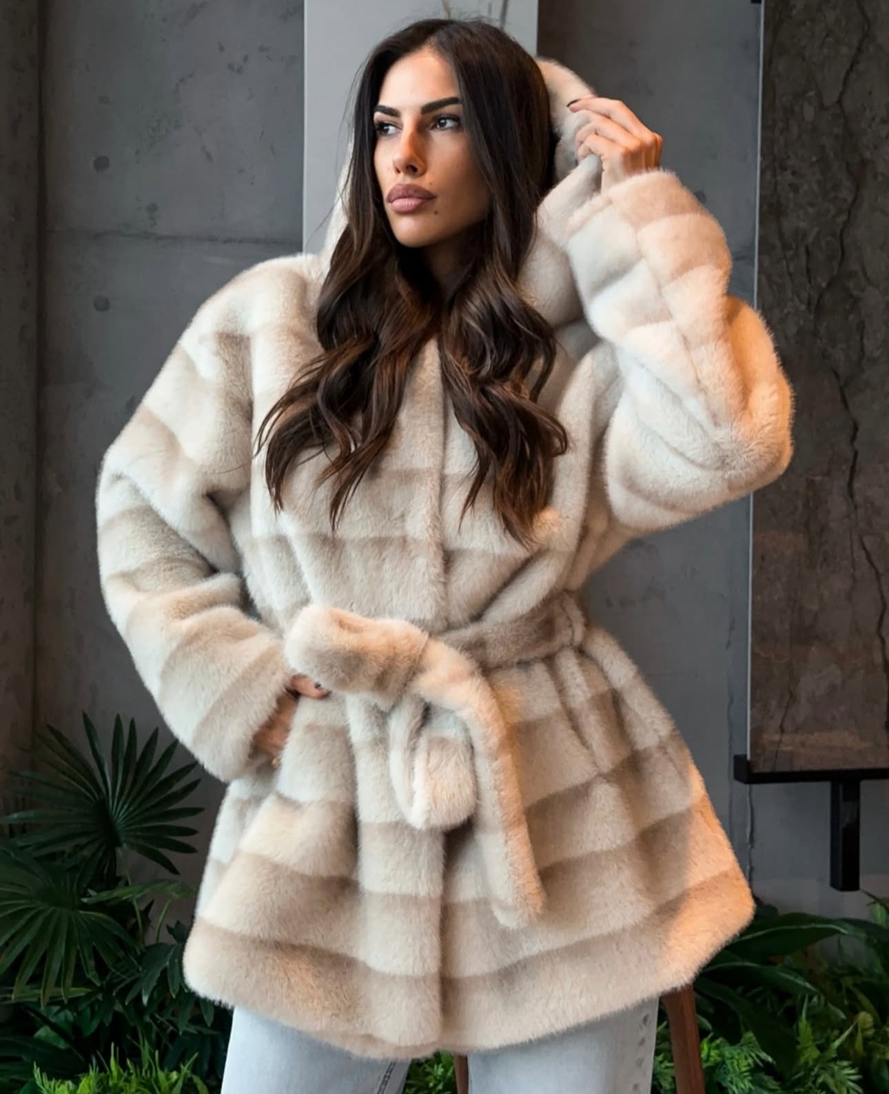Pelliccia GEMMA Realizzato in pelliccia di visone ecologico di alta qualità, presenta una texture morbida e avvolgente con lavorazione a fasce orizzontali. Il design è arricchito da cappuccio e cintura in coordinato