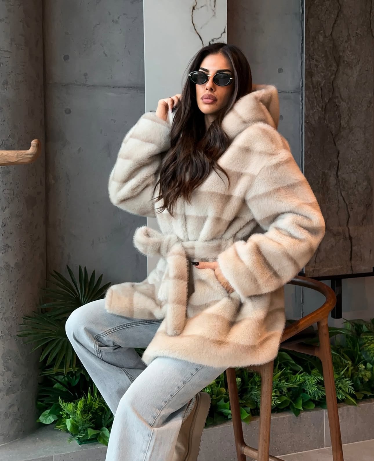 Pelliccia GEMMA Realizzato in pelliccia di visone ecologico di alta qualità, presenta una texture morbida e avvolgente con lavorazione a fasce orizzontali. Il design è arricchito da cappuccio e cintura in coordinato