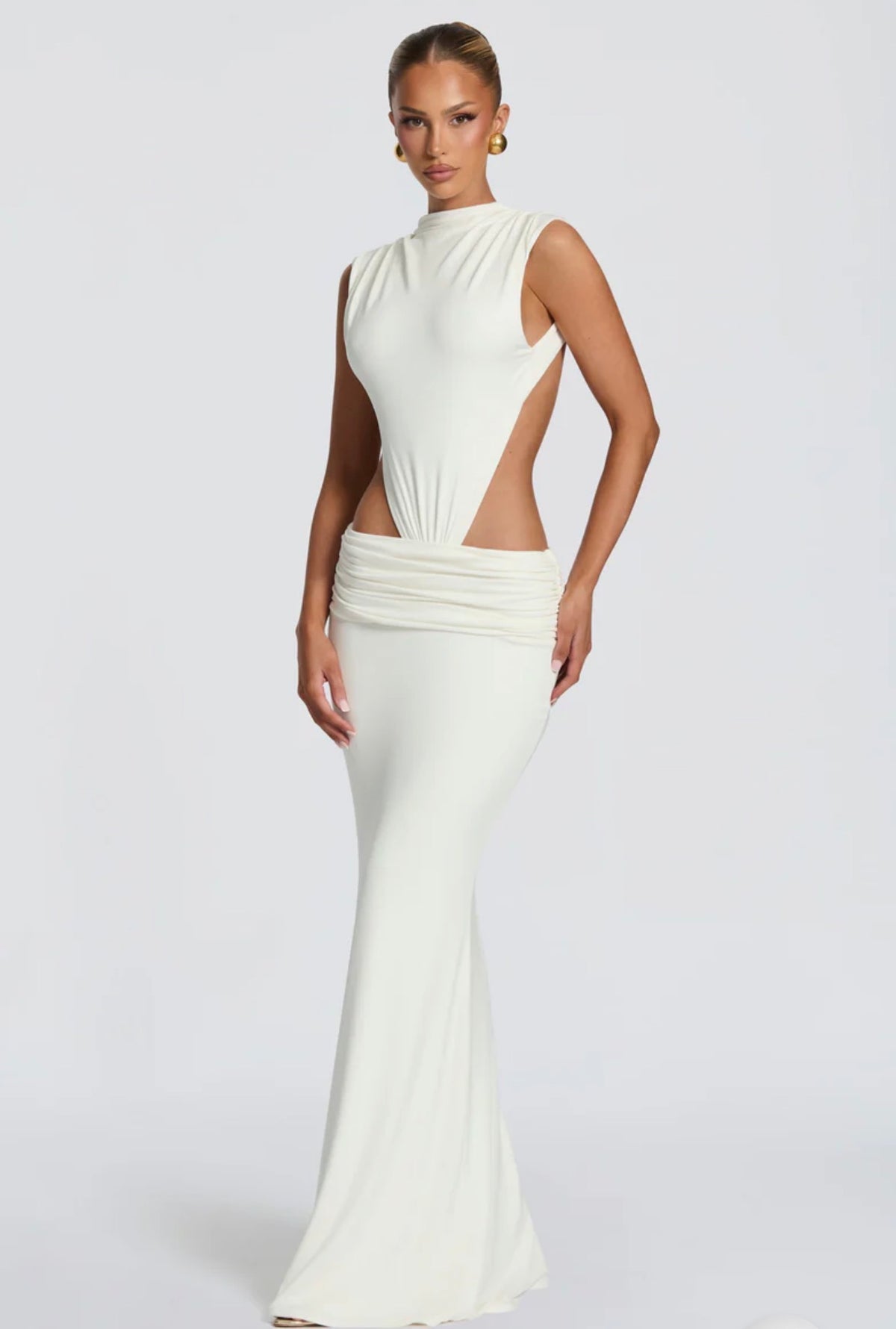 Abito Sahara maxi aderente  con design cut-out laterale che scolpisce la silhouette. Il collo alto crea un raffinato contrasto con le ampie aperture sui fianchi e la schiena scoperta, per un effetto sensuale ma sofisticato.