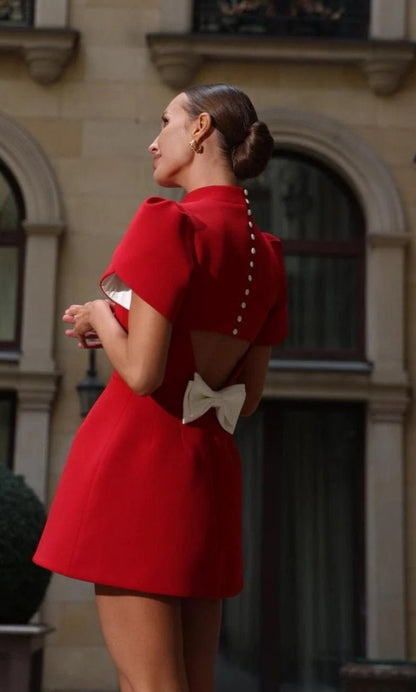 Mini Dress ALICE e sofisticato con maniche corte a sbuffo e una chiusura posteriore con bottoni  rivestiti di perle, che aggiungono un tocco raffinato. La parte posteriore ha un'apertura che lascia intravedere la schiena, valorizzata da un fiocco