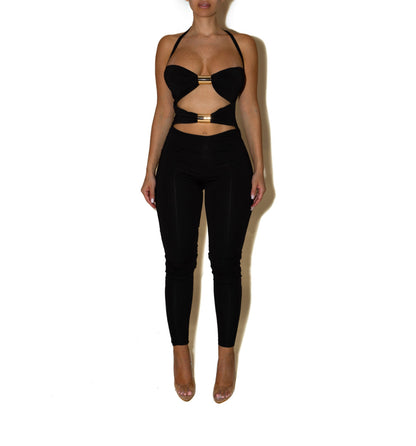 Jumpsuite SCARLETT Un look audace e raffinato che valorizza la silhouette con un design cut-out e dettagli metallici. Il top con inserti dorati e il pantalone a vita alta creano un equilibrio perfetto tra sensualità e stile moderno.