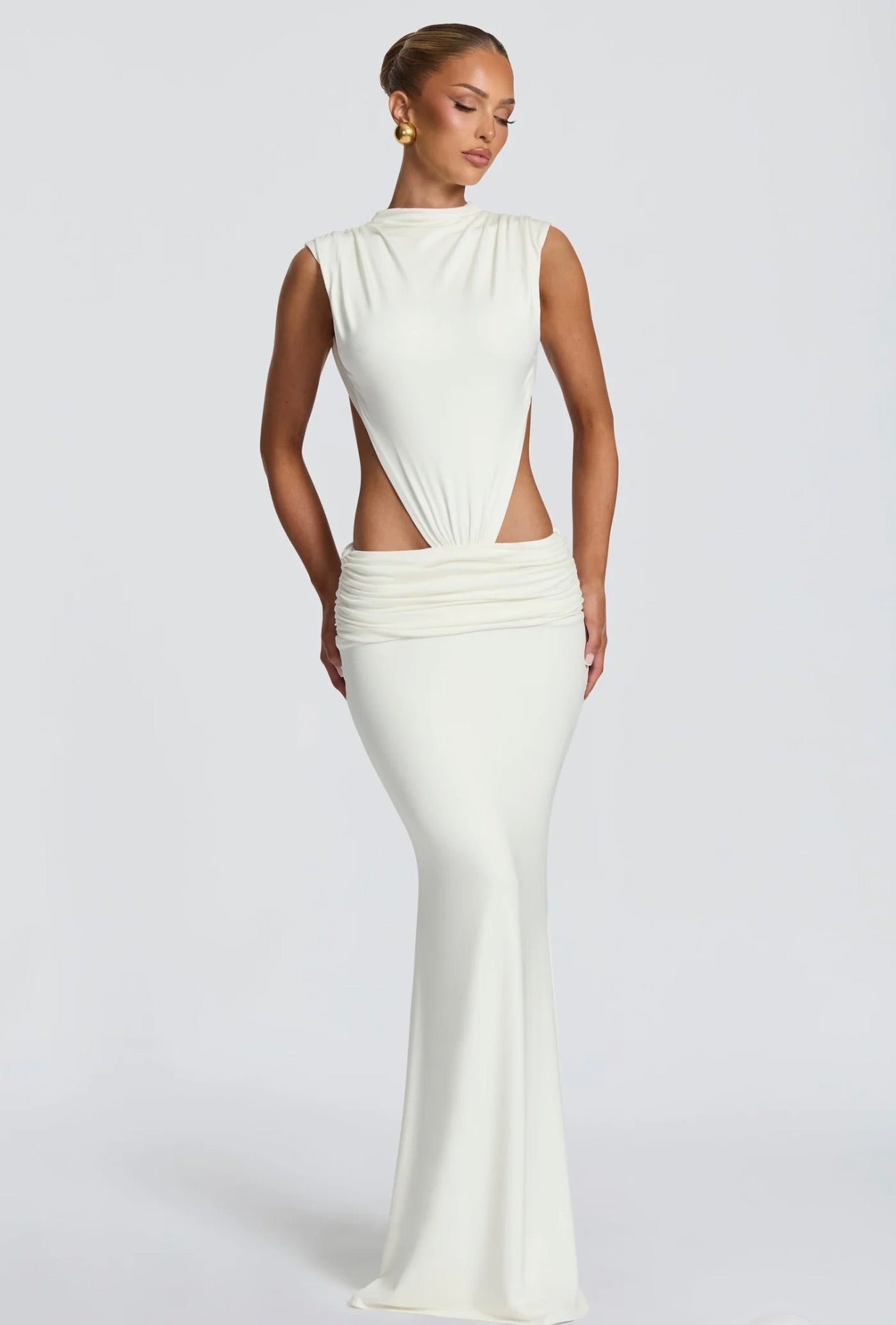 Abito Sahara maxi aderente  con design cut-out laterale che scolpisce la silhouette. Il collo alto crea un raffinato contrasto con le ampie aperture sui fianchi e la schiena scoperta, per un effetto sensuale ma sofisticato.