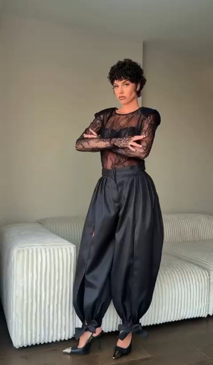 Outfit Gabriella elegante e sensuale composto da maglia in pizzo trasparente e pantalone nero a vita alta. Il pantalone presenta una linea fluida con spacco laterale e dettagli con fiocchi alla caviglia, per un look sofisticato e di grande impatto.