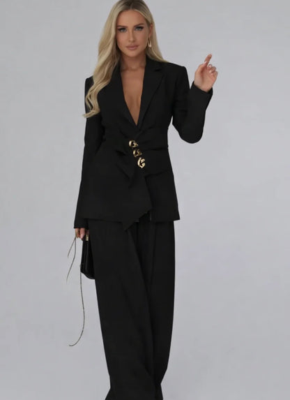 Tailleur Letizia composto da blazer strutturato con chiusura asimmetrica bottoni gioiello e pantaloni palazzo fluidi. Linee raffinate che valorizzano la silhouette, perfetto per occasioni chic o outfit da giorno sofisticati.