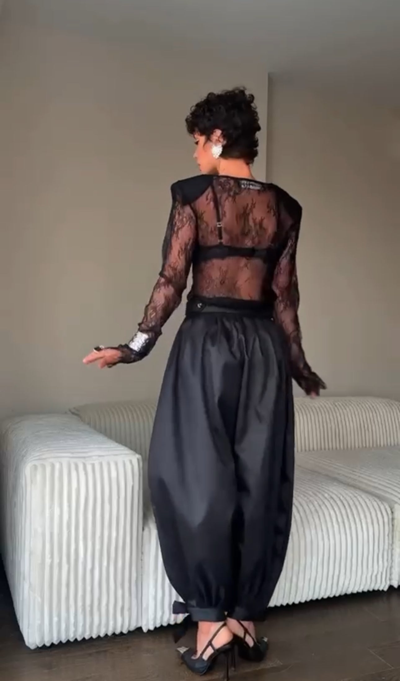 Outfit Gabriella elegante e sensuale composto da maglia in pizzo trasparente e pantalone nero a vita alta. Il pantalone presenta una linea fluida con spacco laterale e dettagli con fiocchi alla caviglia, per un look sofisticato e di grande impatto.