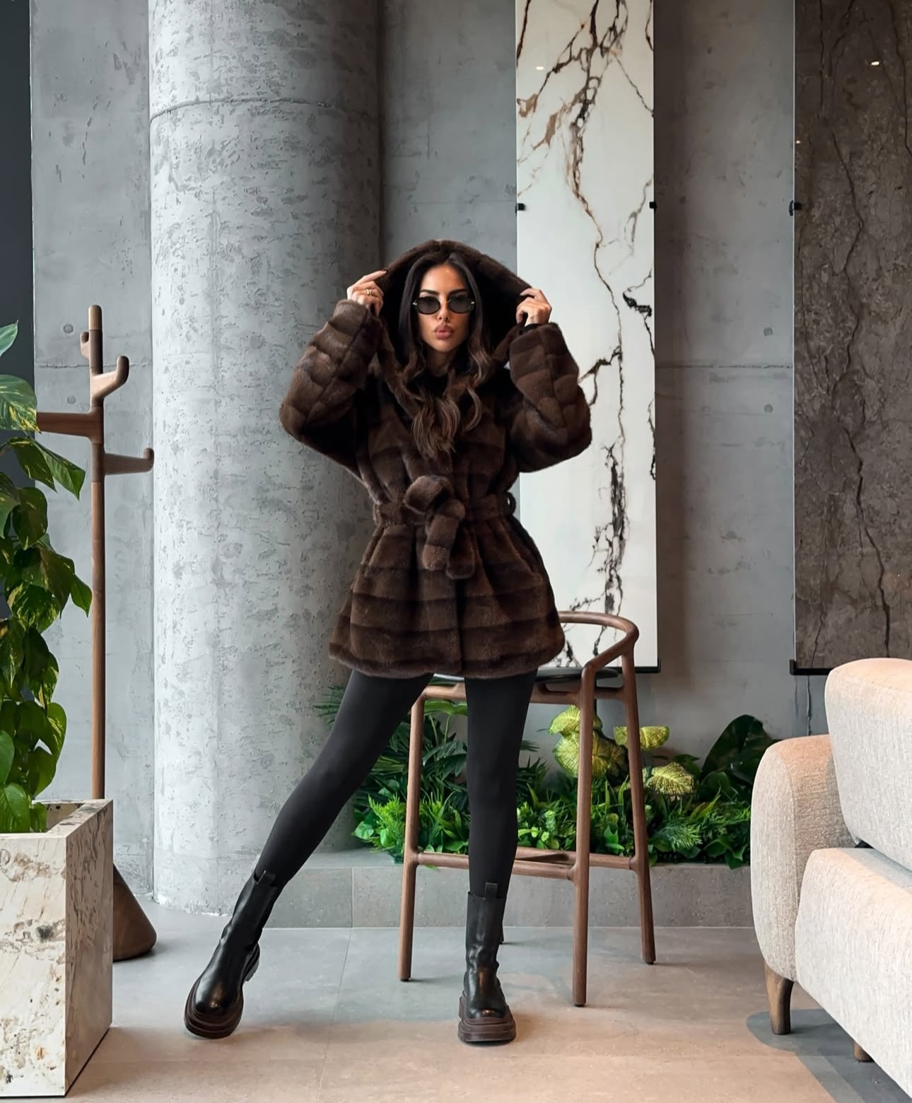 Pelliccia GEMMA Realizzato in pelliccia di visone ecologico di alta qualità, presenta una texture morbida e avvolgente con lavorazione a fasce orizzontali. Il design è arricchito da cappuccio e cintura in coordinato