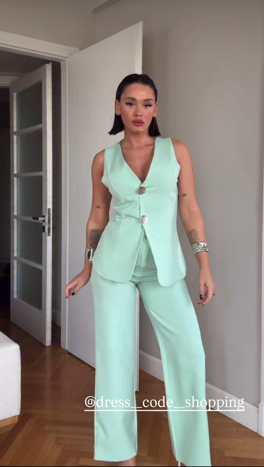 Tailleur ESTER elegante composto da un gilet smanicato e un paio di pantaloni a gamba larga  Il gilet presenta due bottoni decorativi centrali dal design gioiello. I pantaloni sono a vita alta, con una vestibilità morbida e fluida