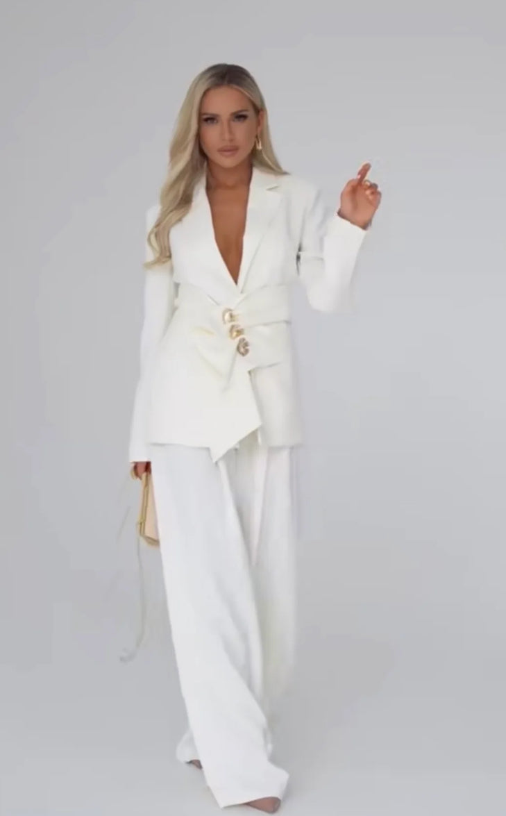 Tailleur Letizia composto da blazer strutturato con chiusura asimmetrica bottoni gioiello e pantaloni palazzo fluidi. Linee raffinate che valorizzano la silhouette, perfetto per occasioni chic o outfit da giorno sofisticati.
