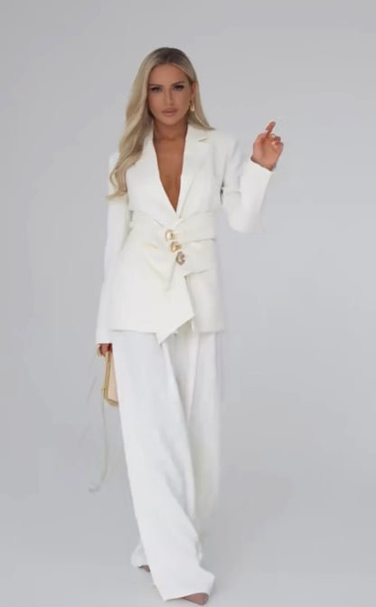 Tailleur Letizia composto da blazer strutturato con chiusura asimmetrica bottoni gioiello e pantaloni palazzo fluidi. Linee raffinate che valorizzano la silhouette, perfetto per occasioni chic o outfit da giorno sofisticati.