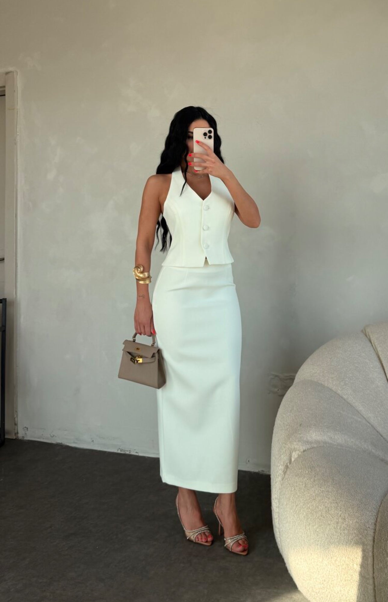 Set ZAIRA indossa un elegante completo bianco composto da un top senza maniche con bottoni e scollo a V, insieme a una gonna a matita lunga fino alla caviglia. Il tessuto di alta qualità