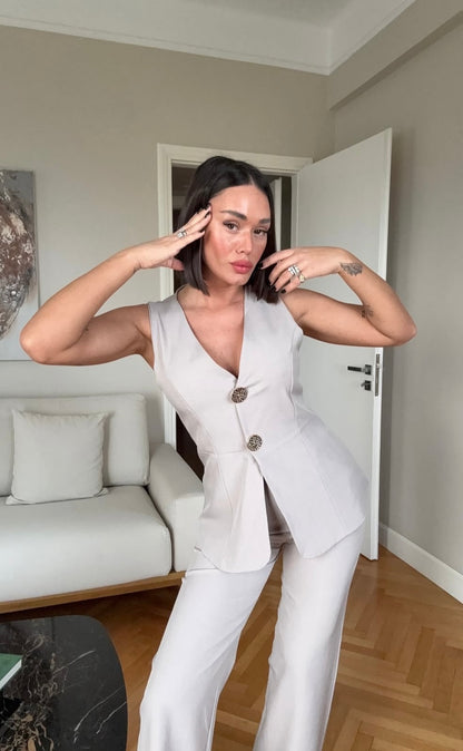 Tailleur ESTER elegante composto da un gilet smanicato e un paio di pantaloni a gamba larga  Il gilet presenta due bottoni decorativi centrali dal design gioiello. I pantaloni sono a vita alta, con una vestibilità morbida e fluida