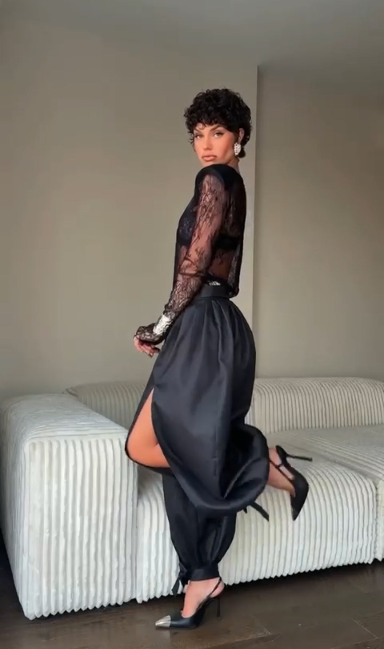 Outfit Gabriella elegante e sensuale composto da maglia in pizzo trasparente e pantalone nero a vita alta. Il pantalone presenta una linea fluida con spacco laterale e dettagli con fiocchi alla caviglia, per un look sofisticato e di grande impatto.