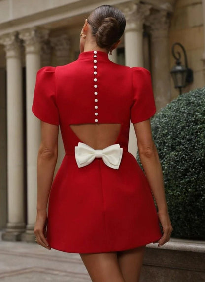 Mini Dress ALICE e sofisticato con maniche corte a sbuffo e una chiusura posteriore con bottoni  rivestiti di perle, che aggiungono un tocco raffinato. La parte posteriore ha un'apertura che lascia intravedere la schiena, valorizzata da un fiocco