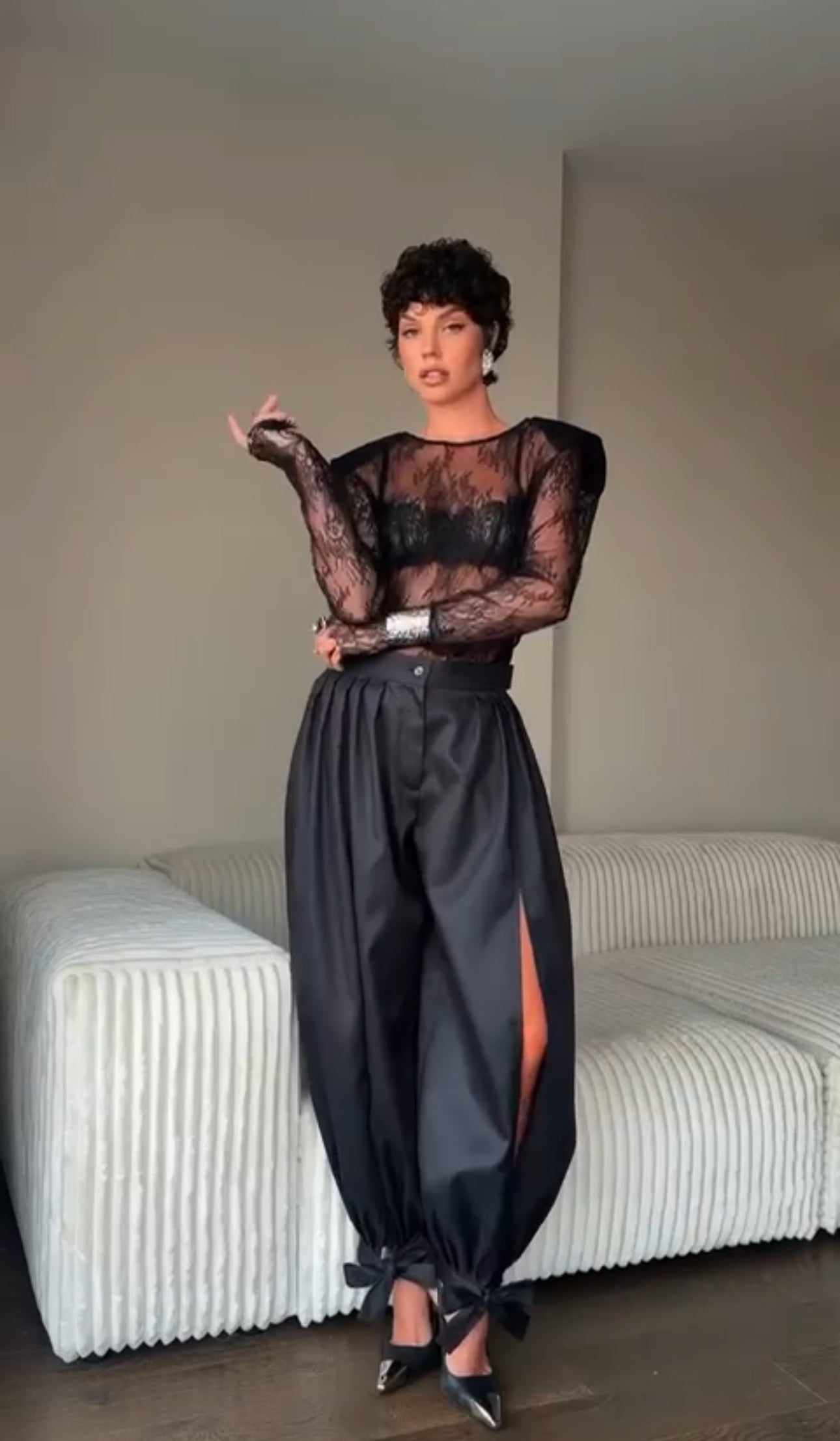 Outfit Gabriella elegante e sensuale composto da maglia in pizzo trasparente e pantalone nero a vita alta. Il pantalone presenta una linea fluida con spacco laterale e dettagli con fiocchi alla caviglia, per un look sofisticato e di grande impatto.