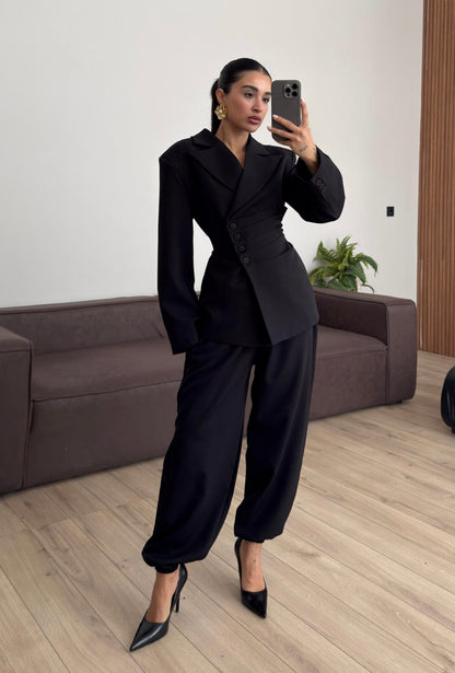 Tailleur Samantha”in promo” composto da giacca sartoriale con spalle strutturate e chiusura incrociata. La cintura integrata con bottoni decorativi stringe il punto vita valorizzando la silhouette e creando un elegante effetto corsetto l pantalone fluido