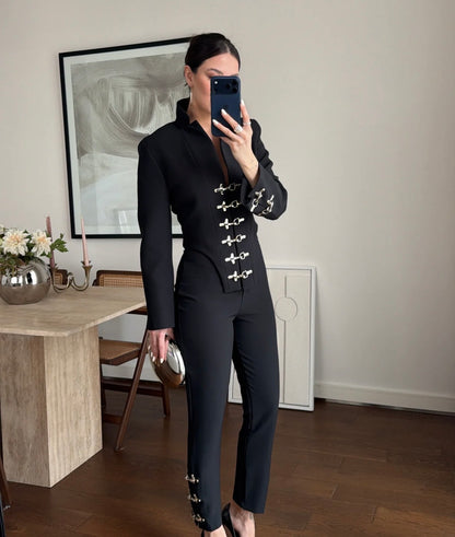 Tailleur Rosella caratterizzato da dettagli in metallo argentato con fibbie decorative sul davanti della giacca e sulla caviglia del pantalone.