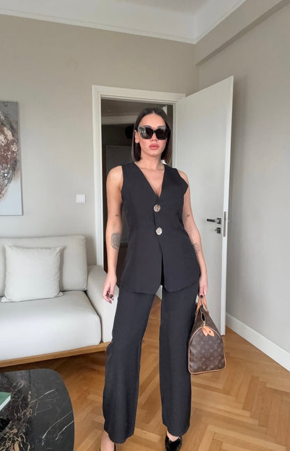 Tailleur ESTER elegante composto da un gilet smanicato e un paio di pantaloni a gamba larga  Il gilet presenta due bottoni decorativi centrali dal design gioiello. I pantaloni sono a vita alta, con una vestibilità morbida e fluida