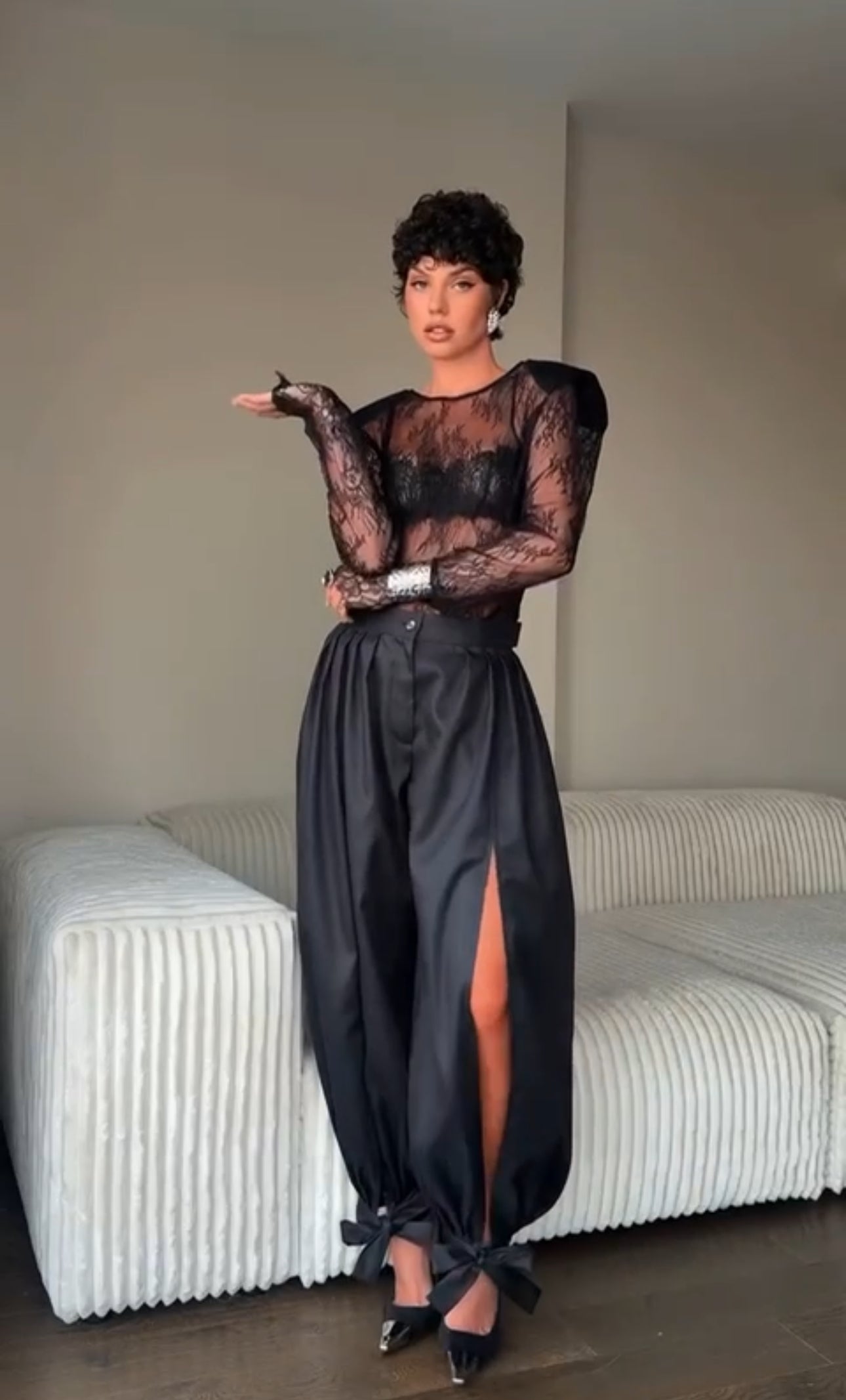 Outfit Gabriella elegante e sensuale composto da maglia in pizzo trasparente e pantalone nero a vita alta. Il pantalone presenta una linea fluida con spacco laterale e dettagli con fiocchi alla caviglia, per un look sofisticato e di grande impatto.