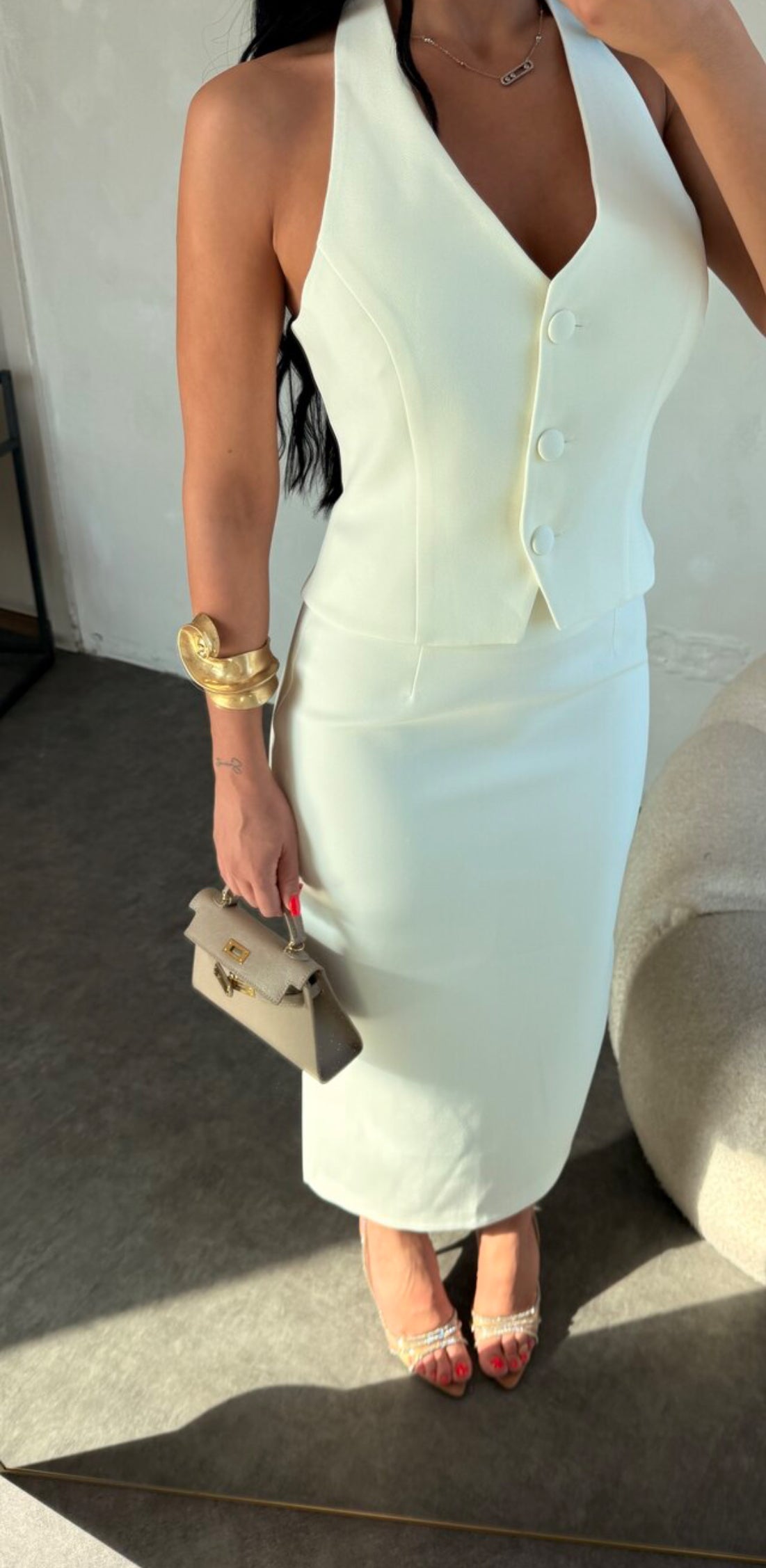 Set ZAIRA indossa un elegante completo bianco composto da un top senza maniche con bottoni e scollo a V, insieme a una gonna a matita lunga fino alla caviglia. Il tessuto di alta qualità