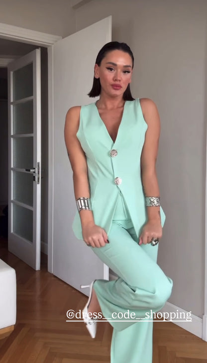 Tailleur ESTER elegante composto da un gilet smanicato e un paio di pantaloni a gamba larga  Il gilet presenta due bottoni decorativi centrali dal design gioiello. I pantaloni sono a vita alta, con una vestibilità morbida e fluida