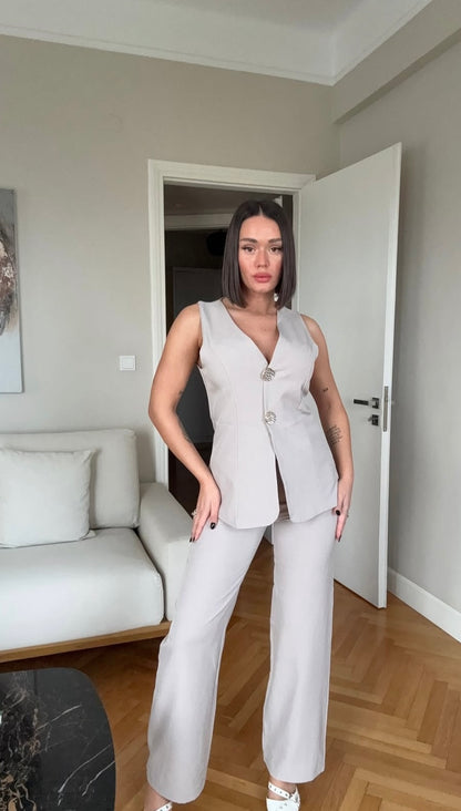 Tailleur ESTER elegante composto da un gilet smanicato e un paio di pantaloni a gamba larga  Il gilet presenta due bottoni decorativi centrali dal design gioiello. I pantaloni sono a vita alta, con una vestibilità morbida e fluida