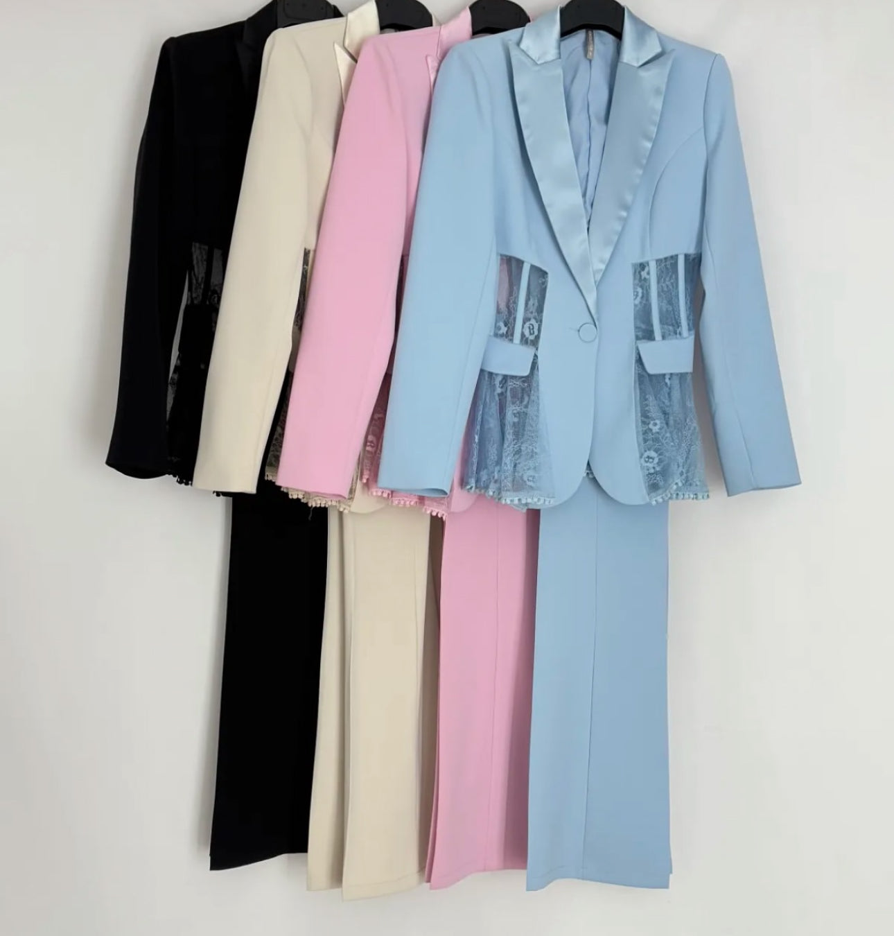 Tailleur MIA elegante composto da blazer e pantaloni coordinati, disponibile in quattro colori raffinati: nero, beige, rosa e azzurro. Il blazer presenta un elegante rever in raso e dettagli in pizzo trasparente sui lati pantalone classico
