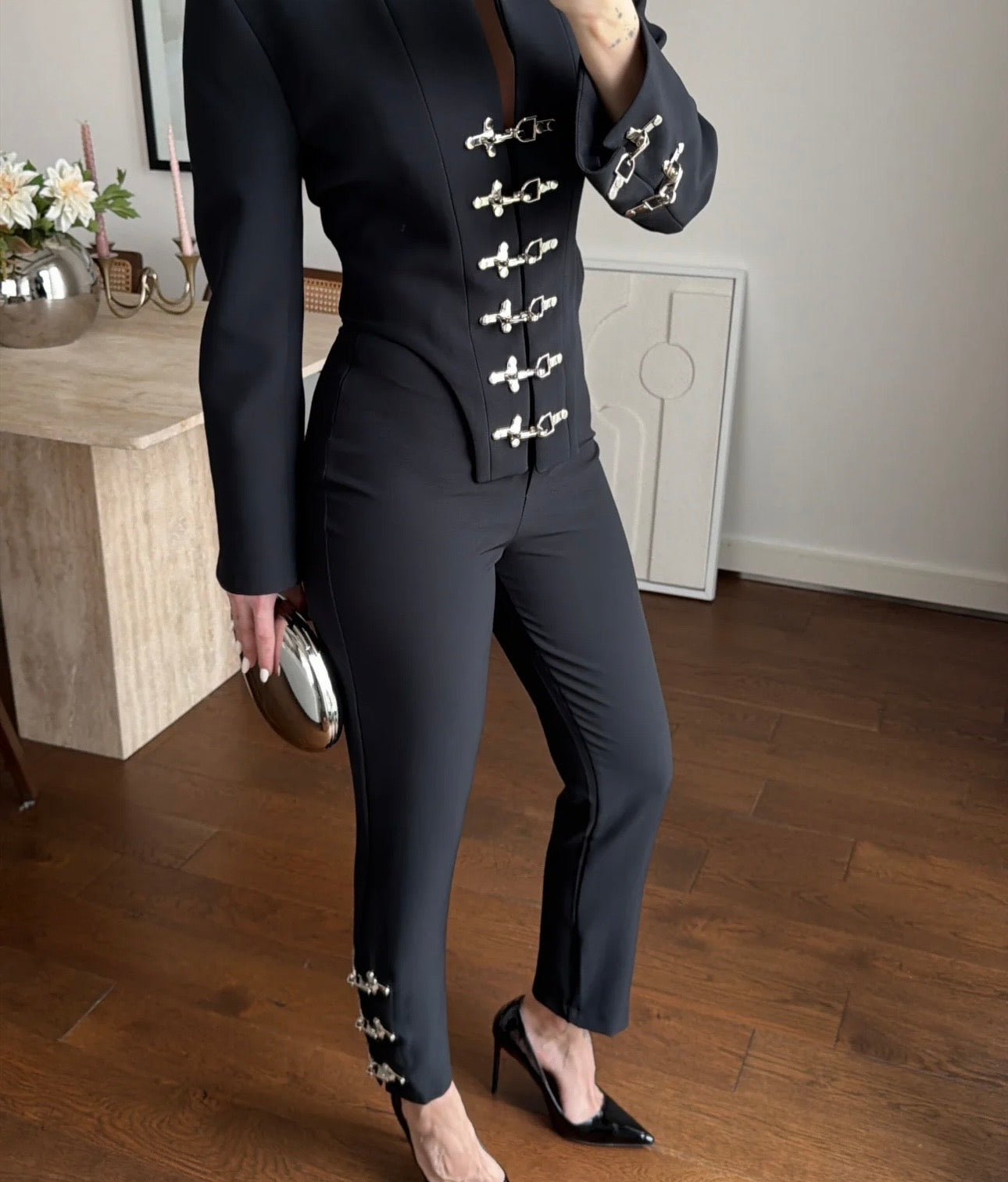 Tailleur Rosella caratterizzato da dettagli in metallo argentato con fibbie decorative sul davanti della giacca e sulla caviglia del pantalone.