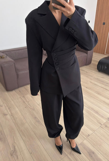 Tailleur Samantha”in promo” composto da giacca sartoriale con spalle strutturate e chiusura incrociata. La cintura integrata con bottoni decorativi stringe il punto vita valorizzando la silhouette e creando un elegante effetto corsetto l pantalone fluido