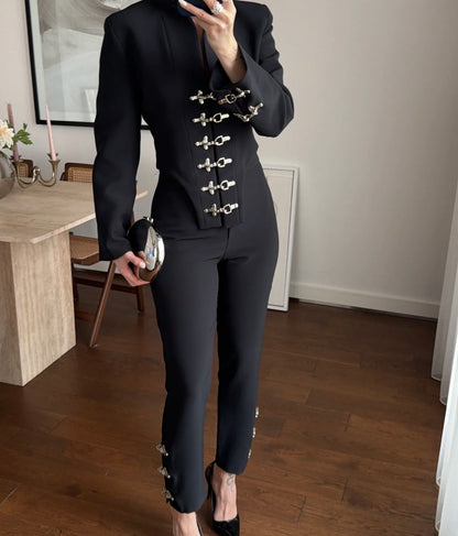 Tailleur Rosella caratterizzato da dettagli in metallo argentato con fibbie decorative sul davanti della giacca e sulla caviglia del pantalone.