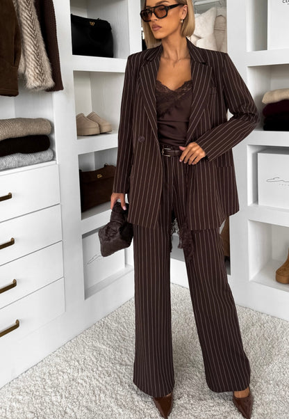 Tailleur Erika sofisticato dal carattere deciso, perfetto per chi ama un’eleganza contemporanea con un tocco sensuale. Il set è composto da blazer doppio petto gessato con top in pizzo e pantalone coordinato a gamba ampia