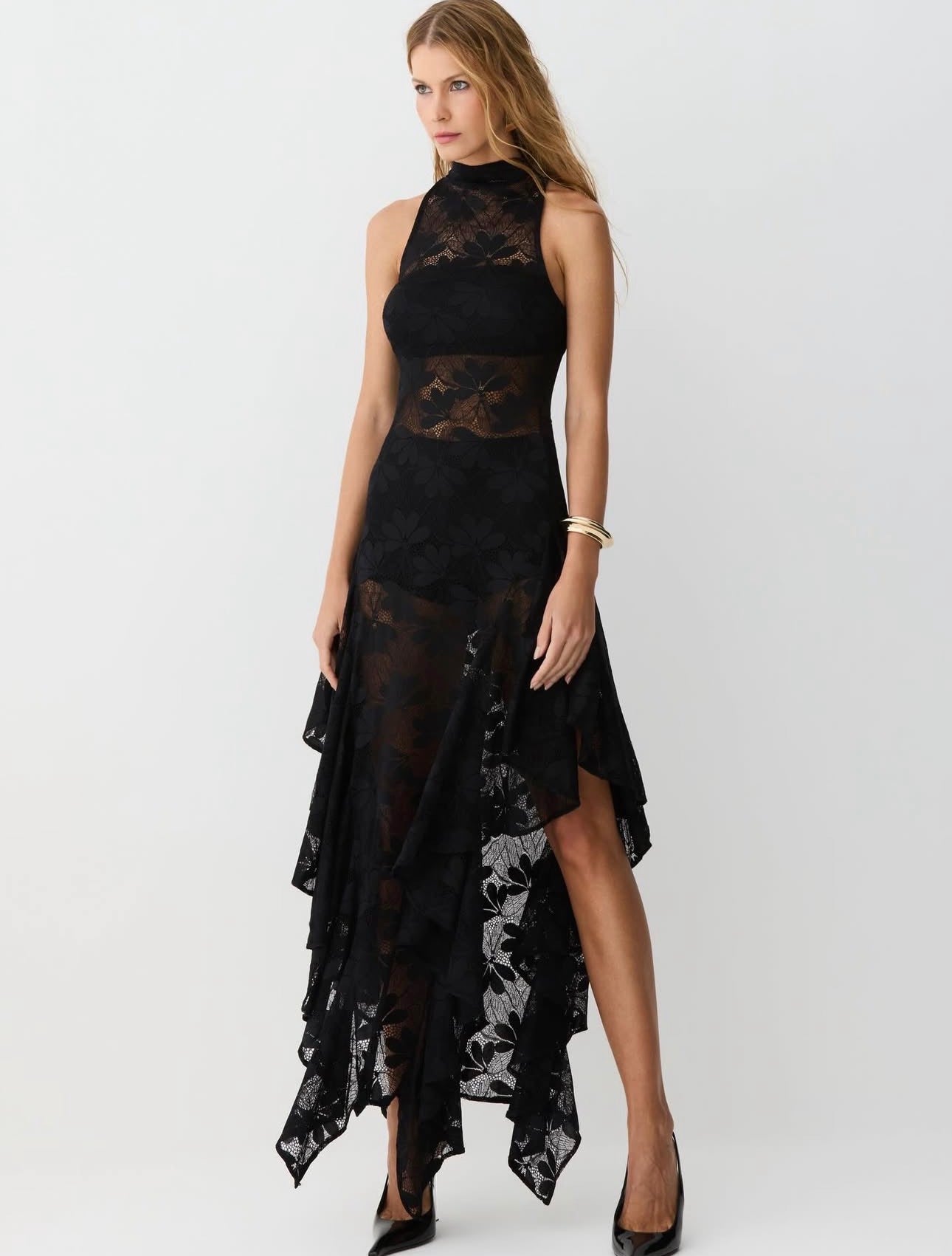 Abito Zaira in pizzo floreale semitrasparente con scollo halter e collo alto. La gonna asimmetrica a strati con orlo a fazzoletto conferisce movimento e carattere, mentre il corpino aderente valorizza la silhouette.